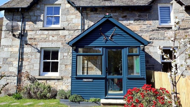 Een stenen huis met een blauwe aanbouw, een schoorsteen en een zonnepaneel.