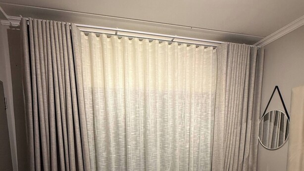 Une chambre d’hôtel avec un lit, des rideaux, une table de chevet, une lampe et un miroir fixé au mur.