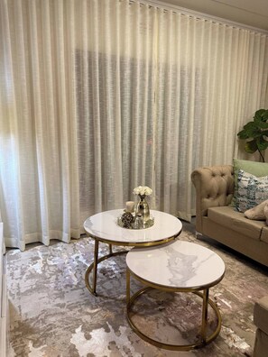 A living room with two round tables, a sofa, and a large window with curtains. - Waterfall Executive suite (Midrand)