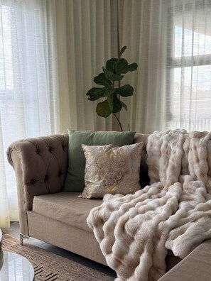 Ein beiges Sofa mit einer gepolsterten Rückenlehne, ein grünes Kissen, ein Zierkissen mit Goldmuster und eine weiße Felldecke.
