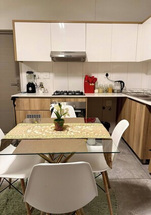 A modern kitchen with white cabinets, a gas stove, a coffee maker, and a dining table with chairs. - Waterfall Executive suite (Midrand)