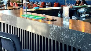 Un espace bar moderne doté d’un comptoir en marbre, de sièges avec coussins et d’un éclairage suspendu.