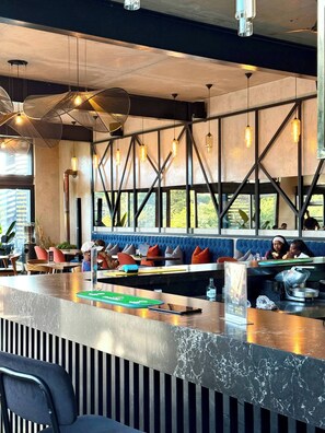 A modern bar area with a marble countertop, seating with cushions, and pendant lighting.