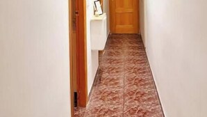 Un couloir étroit, avec une porte en bois au fond, des murs blancs et un sol carrelé.