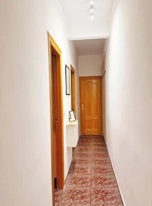 A narrow hallway with a wooden door at the end, white walls, and a tiled floor. - Casa Camila (Los Alcázares)
