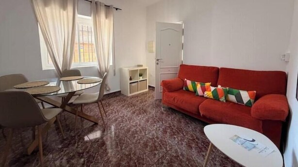 Une pièce comprenant une table à manger, des chaises, un canapé rouge, une petite table blanche et une porte.