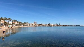 Une plage avec une eau cristalline, des palmiers et des bâtiments en arrière-plan.