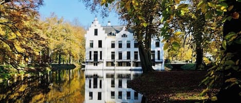 A white building with multiple windows and a reflection in a calm body of water.