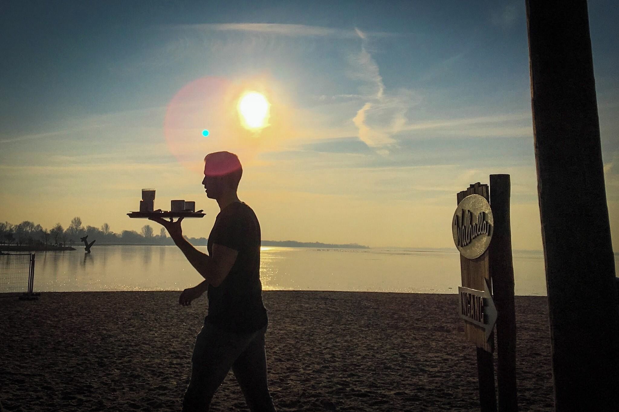 A person carrying trays on a beach with a sunset in the background.