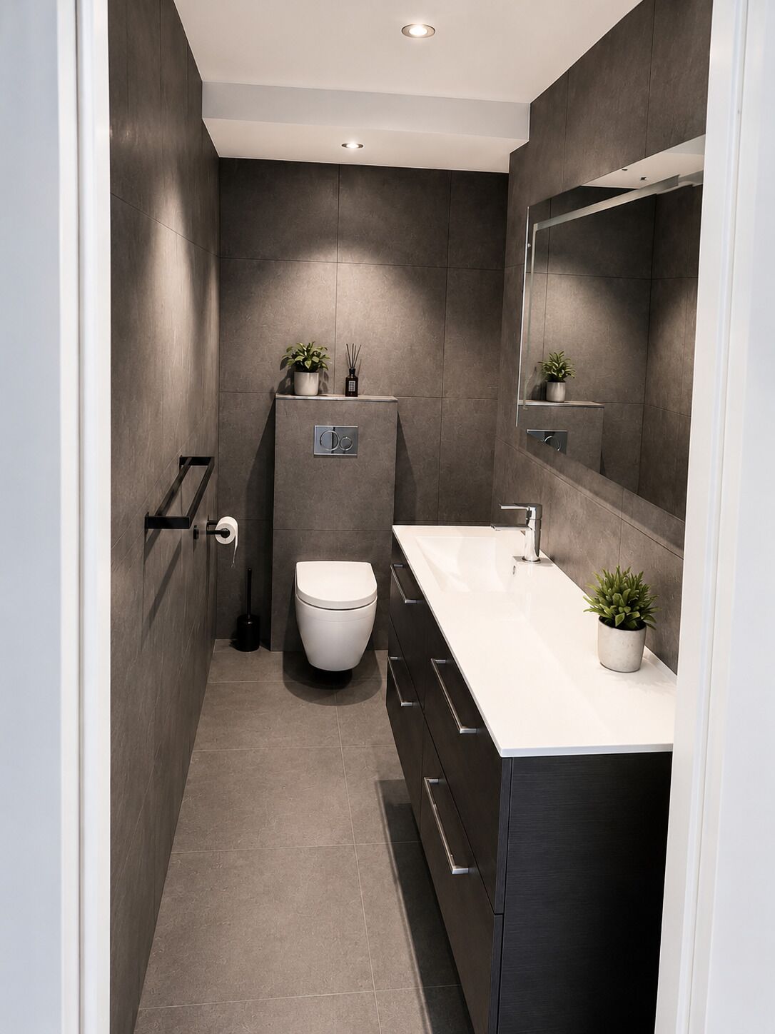 Et moderne badeværelse med en hvid vask, mørke skabe, et toilet og et spejl.
