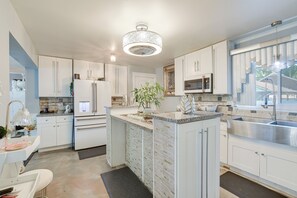 A modern kitchen with white cabinetry, a central island, stainless steel appliances, and a large window providing natural light. - Near Parks & Eats! Elegant Southwest Chicago Home (Chicago)