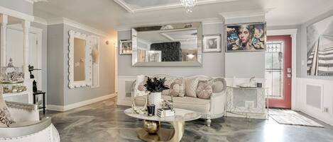 A spacious living room with a chandelier, a white sofa, a coffee table, and a large mirror.