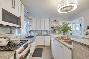 Une cuisine moderne avec des meubles blancs, une cuisinière en acier inoxydable et un grand îlot central agrémenté d’une plante.
