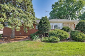 A single-story house with a brick exterior, a front yard with various trees and shrubs, and a clear sky. - Near Parks & Eats! Elegant Southwest Chicago Home (Chicago)