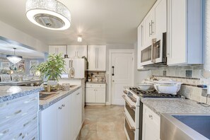 A kitchen with white cabinets, a stove, a microwave, and a chandelier. - Near Parks & Eats! Elegant Southwest Chicago Home (Chicago)