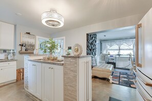 A modern kitchen with white cabinetry, a central island, and a dining area with a tufted sofa. - Near Parks & Eats! Elegant Southwest Chicago Home (Chicago)