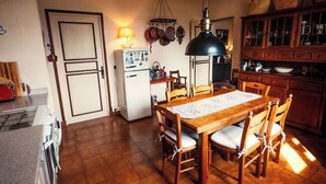 A kitchen with a dining table, chairs, a refrigerator, a hanging light fixture, and wooden cabinets. - Book your stay at Villa Bella Vista, Liguria (Apricale)