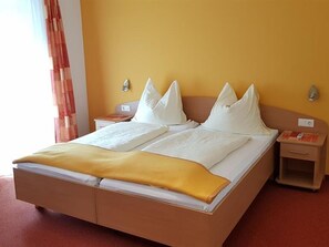 Ein Doppelbett mit weißer Bettwäsche und einer gelben Tagesdecke, ein Nachttisch mit Lampe sowie ein Beistelltischchen mit Telefon.