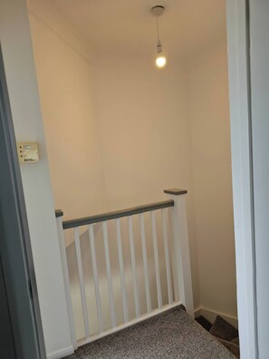A staircase with a white railing and a light fixture above. - The Chilux stylish apartment (Rainham)