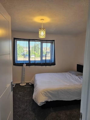 A bedroom with a bed, a standing heater, a window with curtains, and a ceiling light fixture. - The Chilux stylish apartment (Rainham)