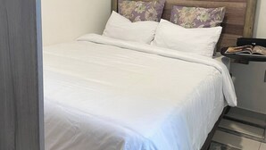 Una cama con ropa de cama blanca, cabecera de madera y almohadas estampadas con motivos florales.