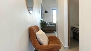 Un pasillo con una silla marrón, un espejo redondo y un sofá al fondo.
