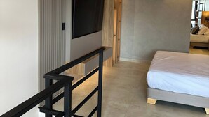 A modern hotel room with a flat-screen TV mounted on the wall, a bed with a white mattress, a wooden floor, and a staircase with a black railing. - Luxury Duplex Loft  AC  Rooftop Jacuzzi Laureles (Medellín)