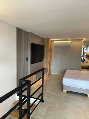 A modern hotel room with a flat-screen TV mounted on the wall, a bed with a white mattress, a wooden floor, and a staircase with a black railing. - Luxury Duplex Loft  AC  Rooftop Jacuzzi Laureles (Medellín)
