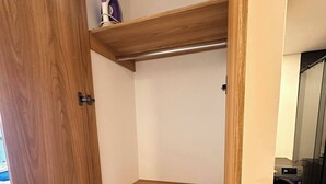Ein Holzschrank mit Ablagefläche und Kleiderstange, ein kleines weißes Objekt auf der Ablagefläche sowie eine Waschmaschine im Hintergrund.
