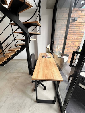 A modern office space with a wooden desk, black metal staircase, and a view of a brick building through a glass door. - Duplex with Incredible View Rooftop Jacuzzi & GYM (Medellín)