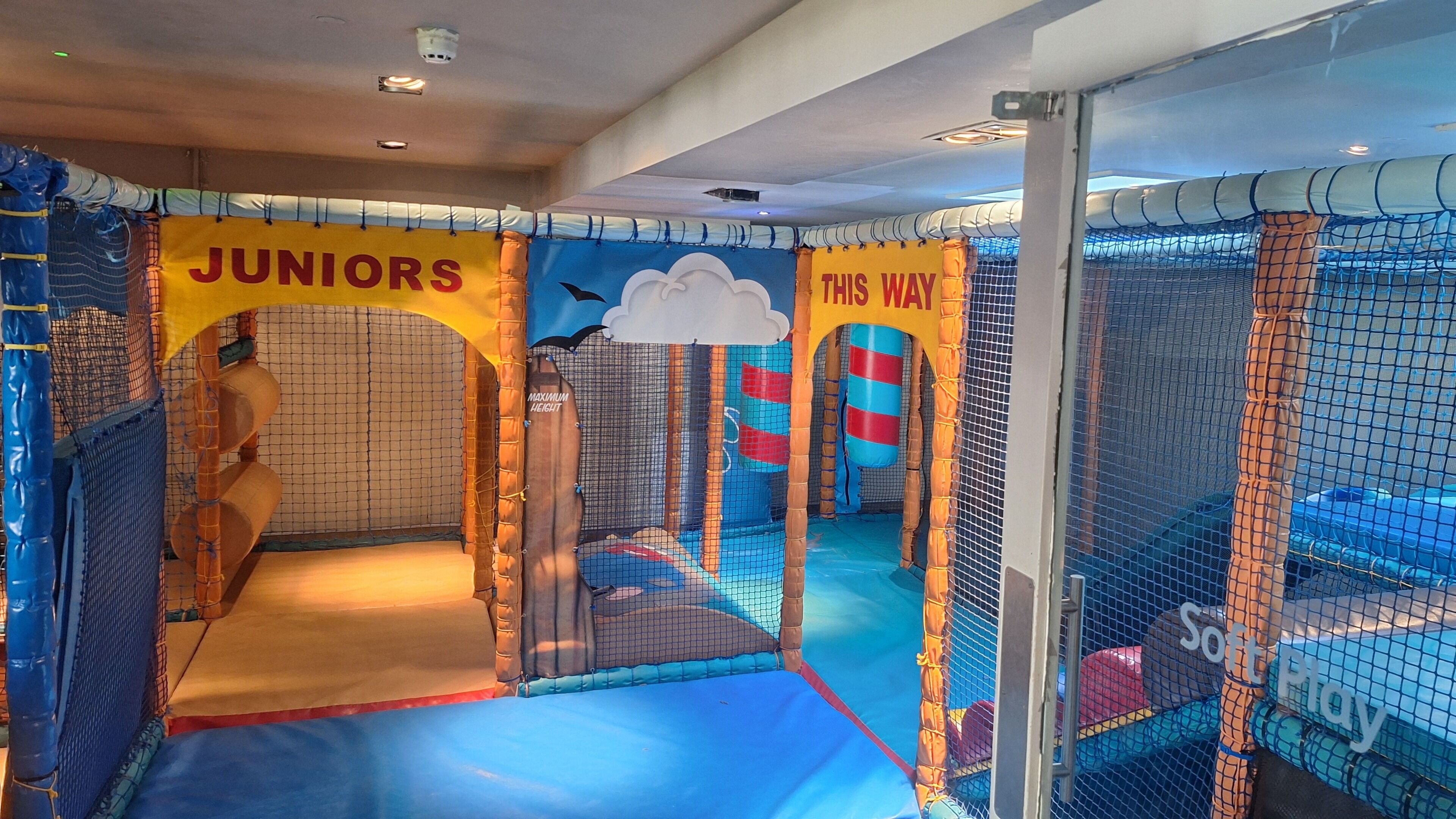 A children's play area with netted walls, a padded floor, and a sign indicating it is for juniors.