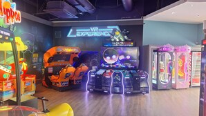 Een ruimte voor VR-gaming met meerdere VR-stations, een groot scherm waarop een spel wordt getoond, en een grijpmachine.