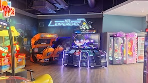 A VR gaming area with multiple VR stations, a large screen displaying a game, and a claw machine. - MKRJ COMFORT PREMIUM PLOT – Sleeps 8 - Pet Friendly - mp276 (Camber)