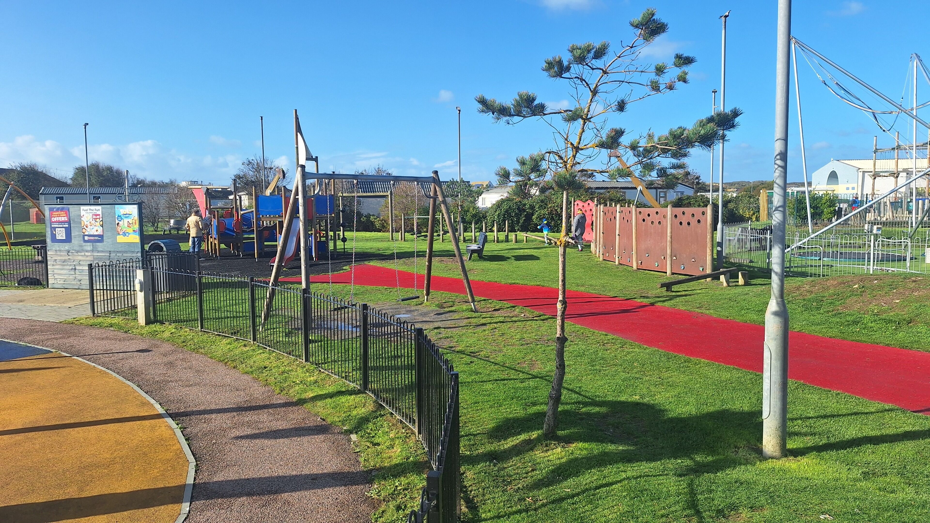 A playground with a red pathway, a small shelter, and a fenced area.