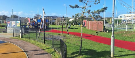 A playground with a red pathway, a small shelter, and a fenced area.