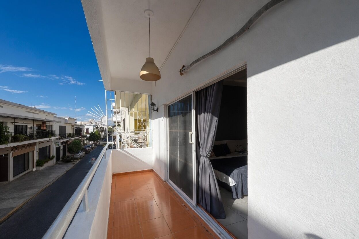 A balcony with a view of a street, a bed with a curtain, and a hanging light fixture.