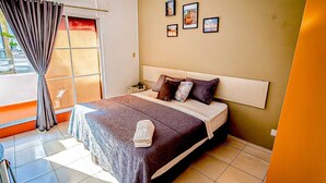 Quarto de hotel com uma cama, mesa de cabeceira, janela com cortinas e parede com quadros.