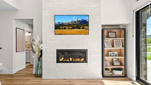 A modern living room with a fireplace, a bookshelf, and a large window.