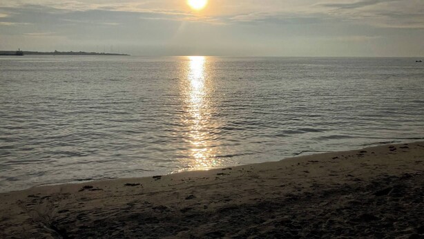Uma praia com mar calmo, horizonte visível e um barco ao longe.