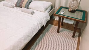 Quarto de hotel com uma cama, mesa de cabeceira com abajur e janela com cortinas.