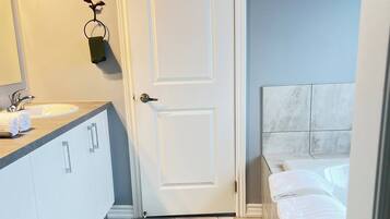 A bathroom with a white door, a sink with a mirror, and a bathtub with towels.