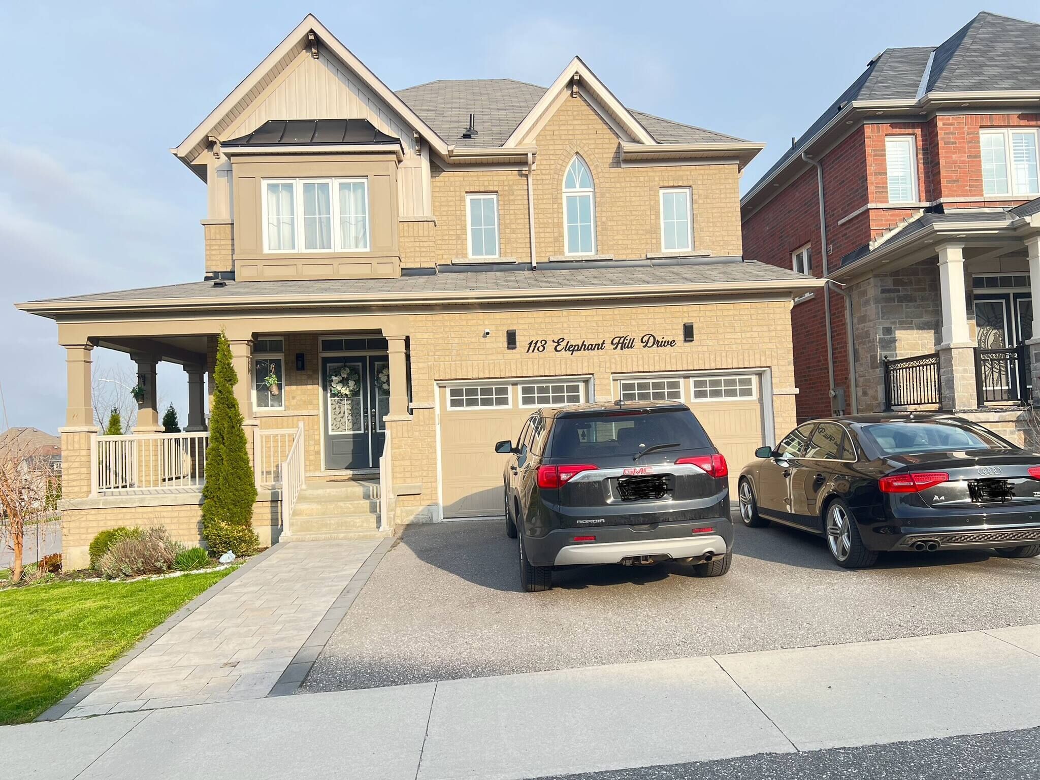 A two-story house with a garage, a driveway, and two parked cars.