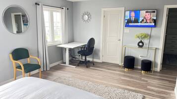 A bedroom with a bed, a desk, a chair, a television, and a door.
