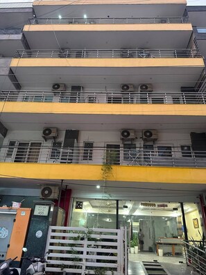 Un edificio de varios pisos con balcones, unidades de aire acondicionado y una entrada con portón.