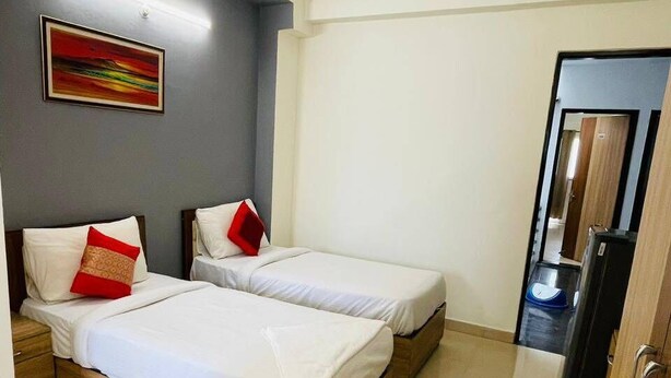 A hotel room with two beds, a ceiling fan, a painting on the wall, and a door leading to a bathroom. - Azalea By Oasis Stays (Gurugram)