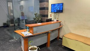 A reception desk with a computer, a plant, and a TV mounted on the wall. - Azalea By Oasis Stays (Gurugram)