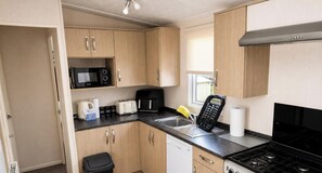 Eine kleine Küche mit Holzschränken, einer Mikrowelle, einem Toaster, einer Kaffeemaschine und einem Herd.