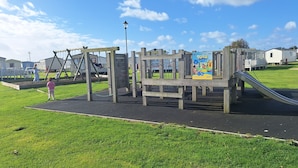 A playground with swings, a slide, and a climbing structure. - MKRJ LUXURY PLUS – Sleeps 8 - Pet Friendly - LARGE En-suite- mp619 (Camber)
