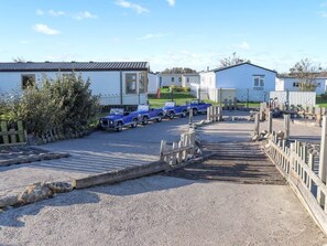 Ein Caravanpark mit mehreren in Reih und Glied stehenden Wohnwagen, einem Kiesparkplatz und einer Holzbrücke, die zu einem eingezäunten Bereich führt.