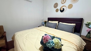 Ein Schlafzimmer mit einem Bett, einem Sessel, einem Nachttisch, einer Wandklimaanlage und Wanddekoration.
